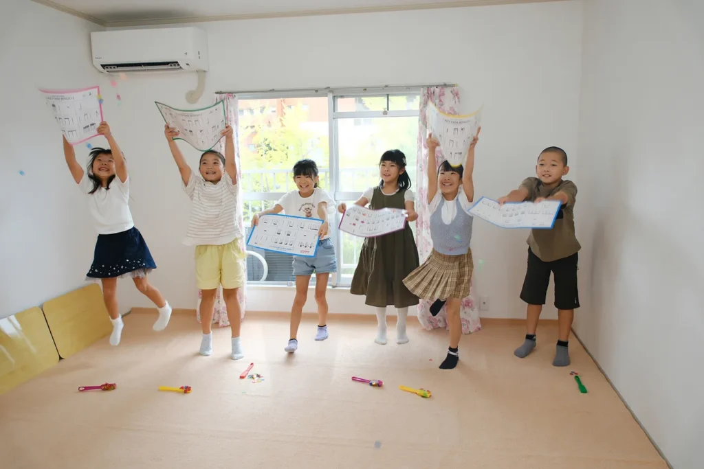 鍵盤表の教材を持って元気にジャンプする子どもたちの音楽教室の一場面